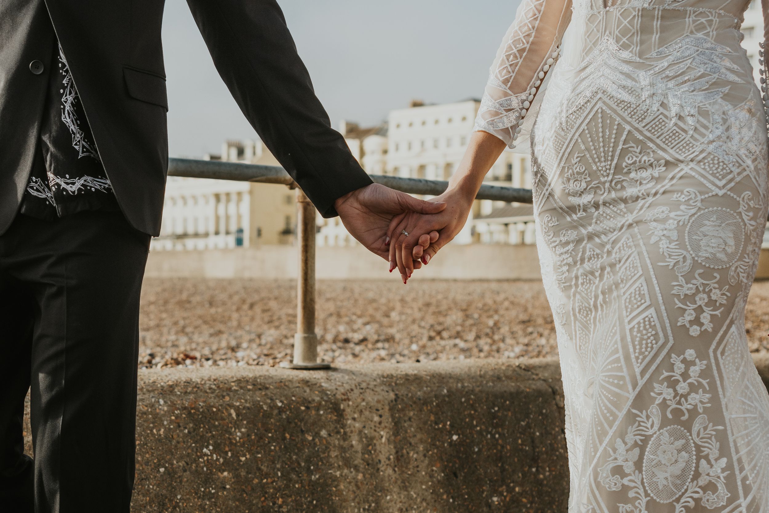 couple walking together holding hands on the beach in Brighton wearing wedding attire