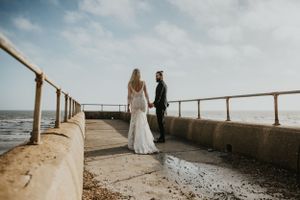 couple walking together holding hands on the beach in Brighton wearing wedding attire