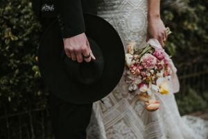 close up of a couple holing flowers and a cowboy hat together wearing wedding clothing in Brighton