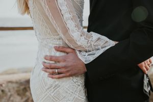 close up of a couples hands as they hold each other wearing wedding attire