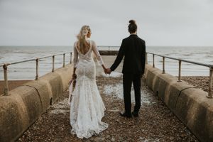 couple walking together holding hands on the beach in Brighton wearing wedding attire