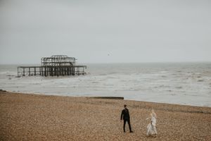 wide shot of a couple wearing wedding attire on Brighton beach by the West Pier
