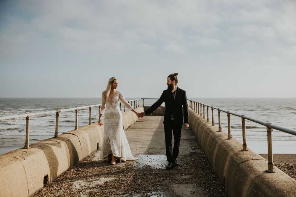 couple walking together holding hands on the beach in Brighton wearing wedding attire