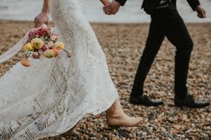 close up of a couple in wedding attire running on the beach holding hands