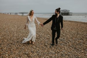 couple running on the beach in wedding attire holding hands in Brighton