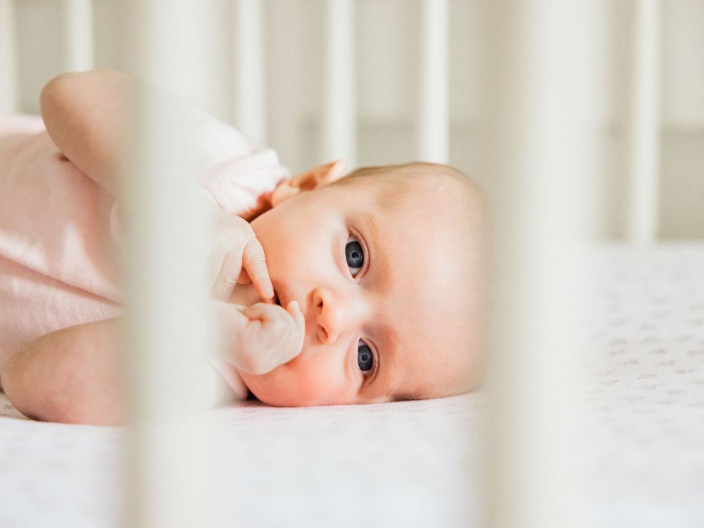infant girl looking through crib slats lifestyle photography