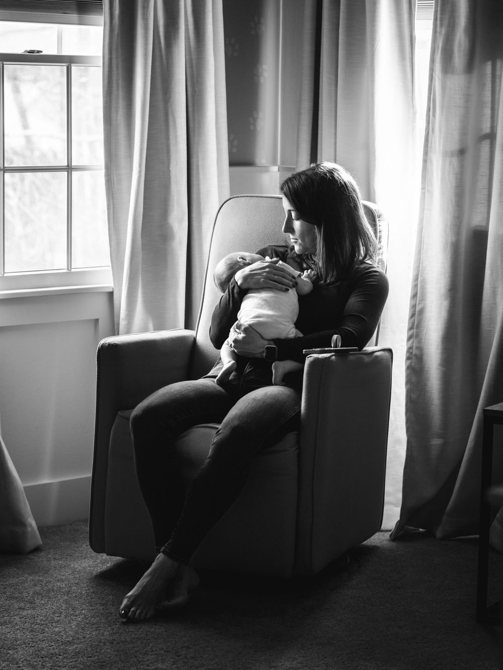 artistic black and white photo of new mother looking at baby in nursery by window