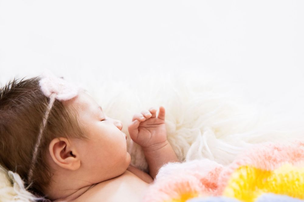 lifestyle portrait of baby sleeping by window in pastel blanket and flower headband