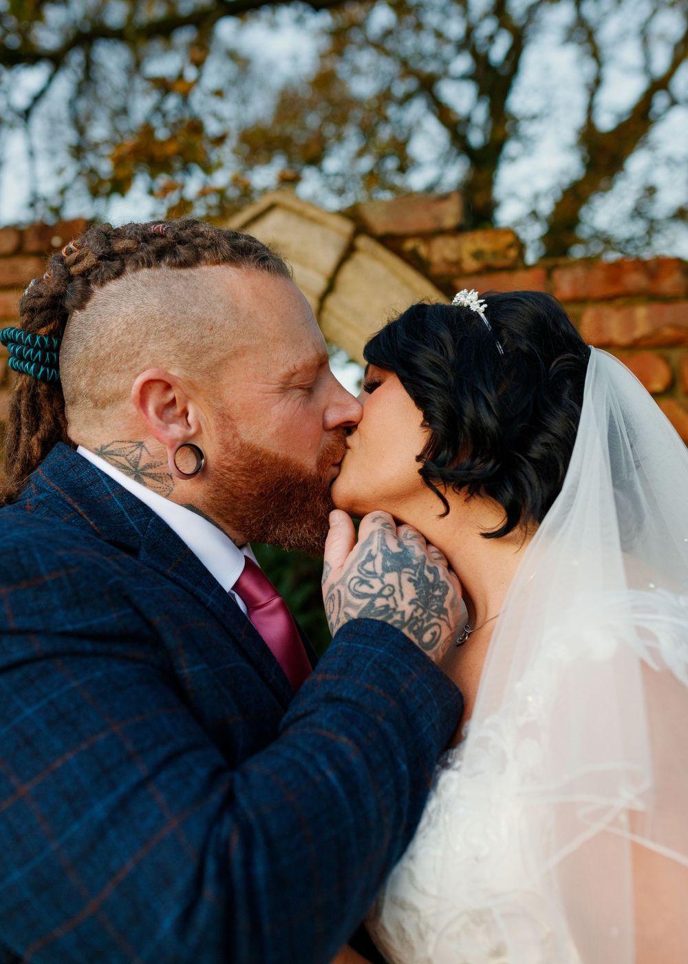 Newlywed couple sharing intimate kiss outdoors under autumn trees.