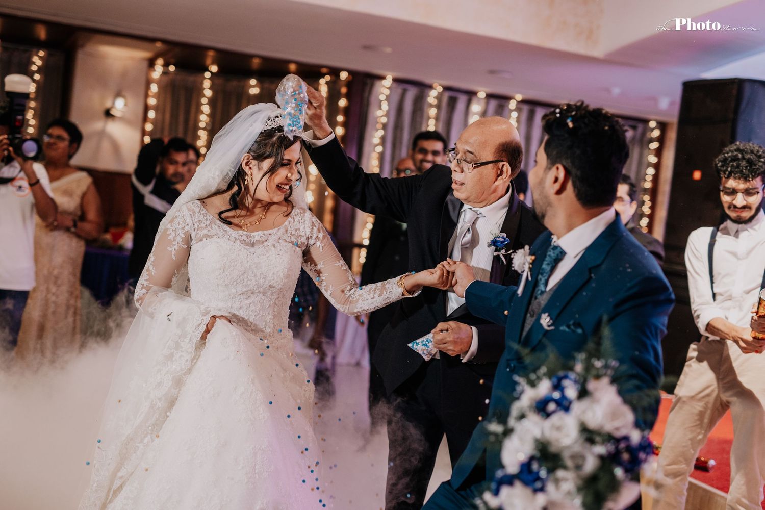 Joyful wedding celebration with guests dancing under decorative lighting and confetti.