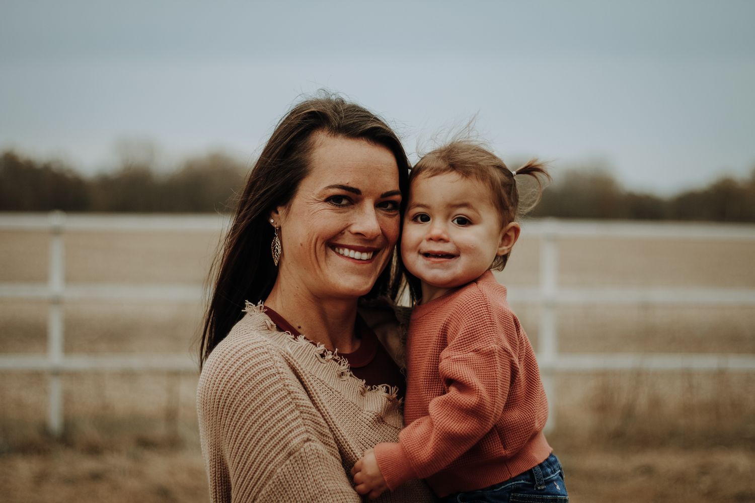 Mother and child sharing joyful moments in autumn field with muted tones.