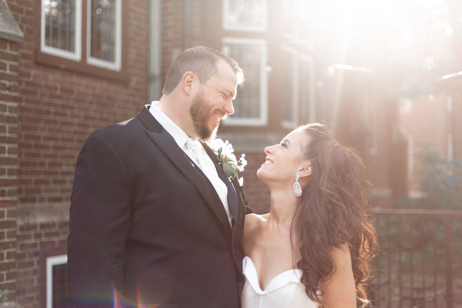 Sunlit close-up of newlyweds sharing an intimate moment against brick building exterior.