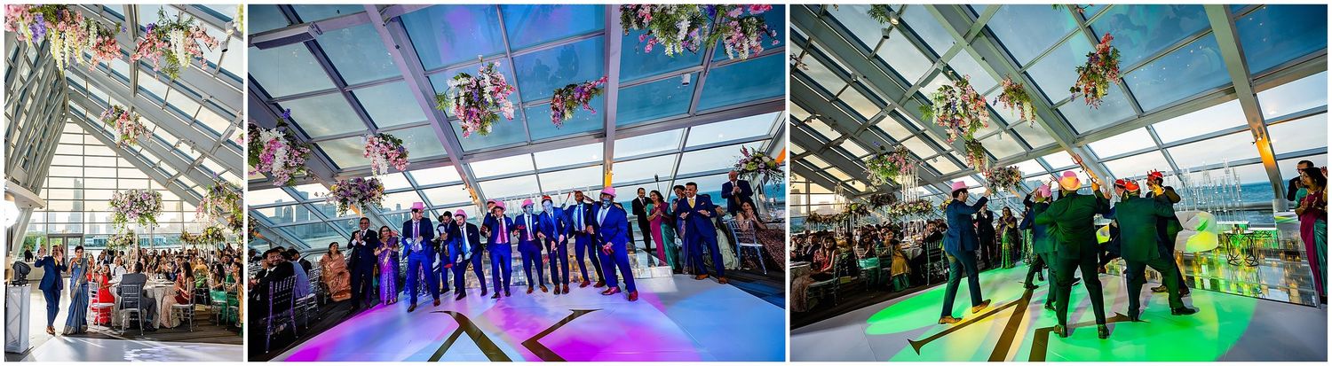 Large group celebration in a glass-enclosed venue with blue lighting and festive atmosphere.