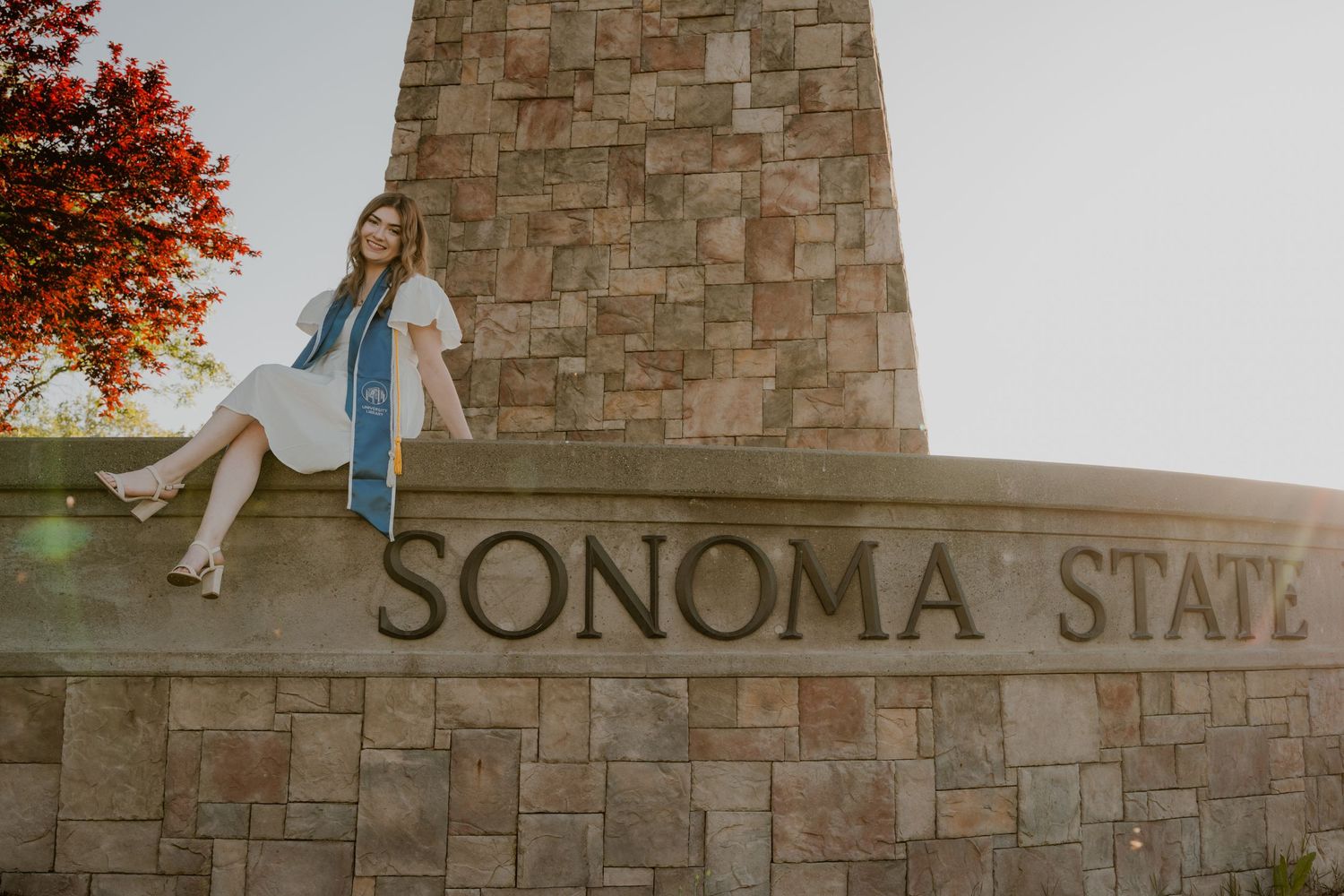 Graduate posing on stone Sonoma State sign during graduation photos.