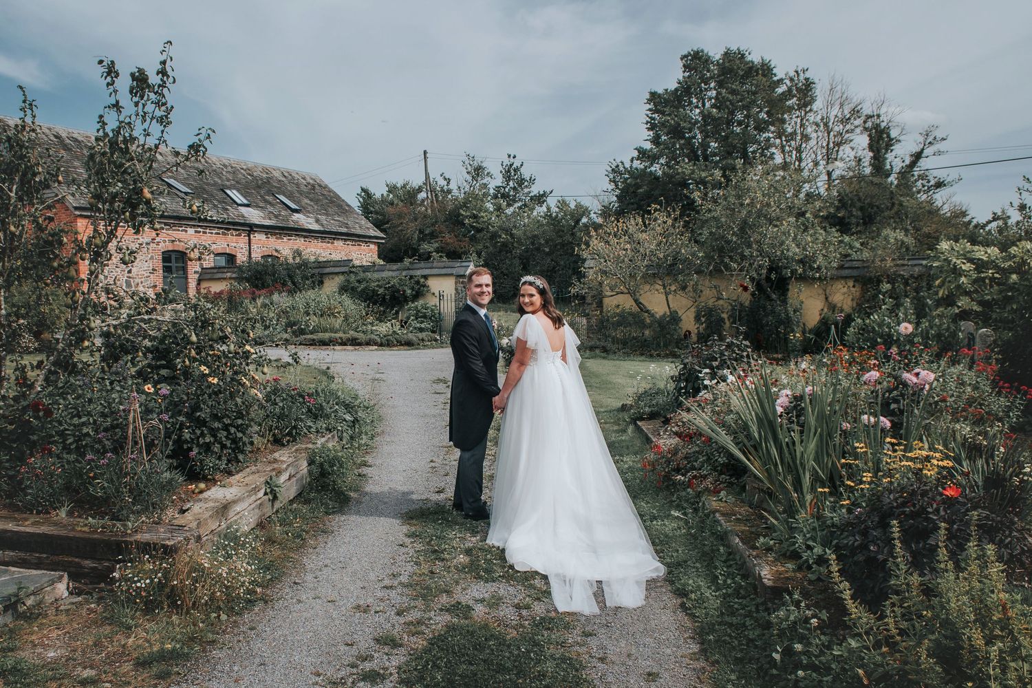 Wedding couple walking hand in hand through the beautiful gardens at The Oak Barn in Devon on their wedding day.