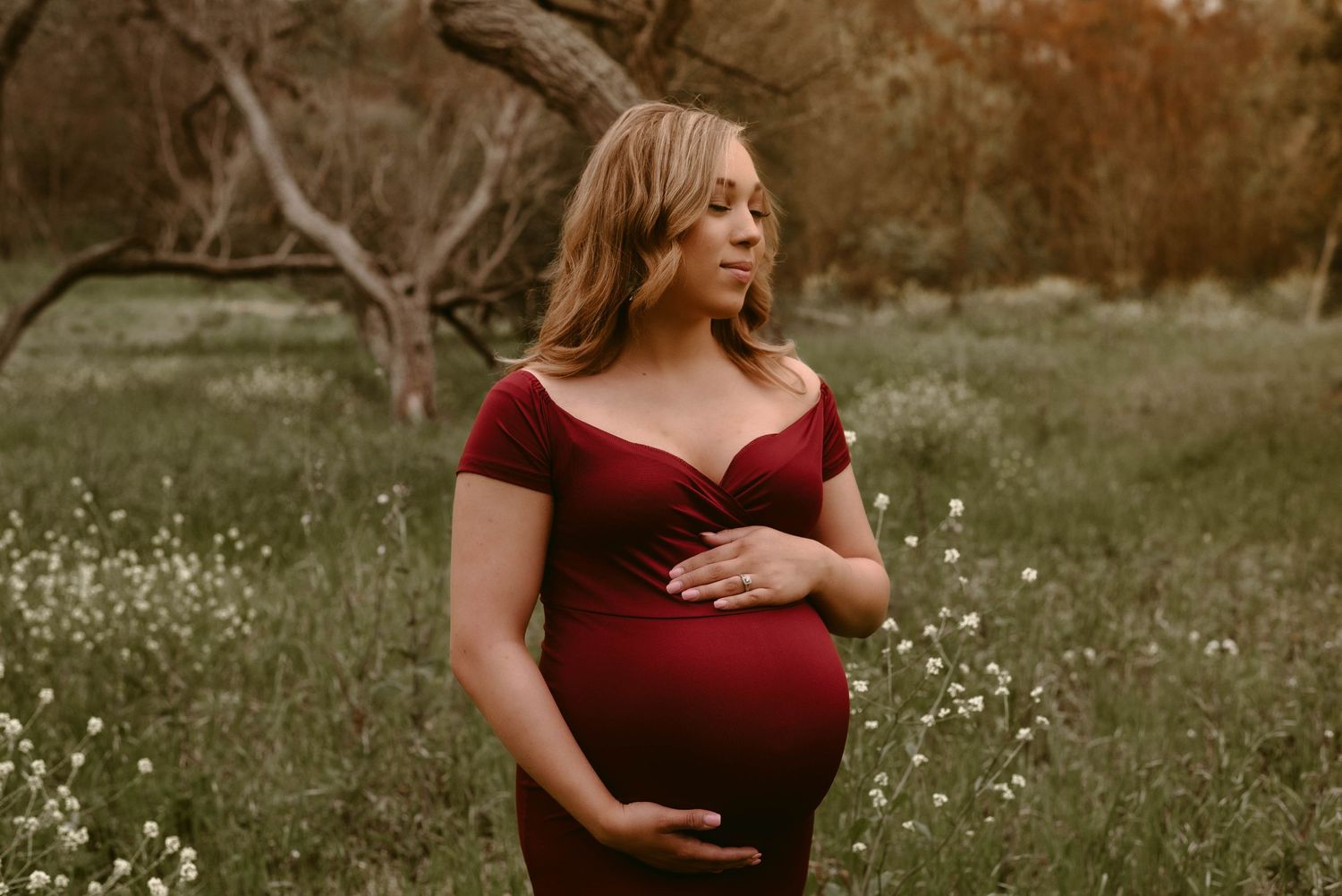 A woman in a burgundy dress poses in a field of wildflowers during a maternity photoshoot.