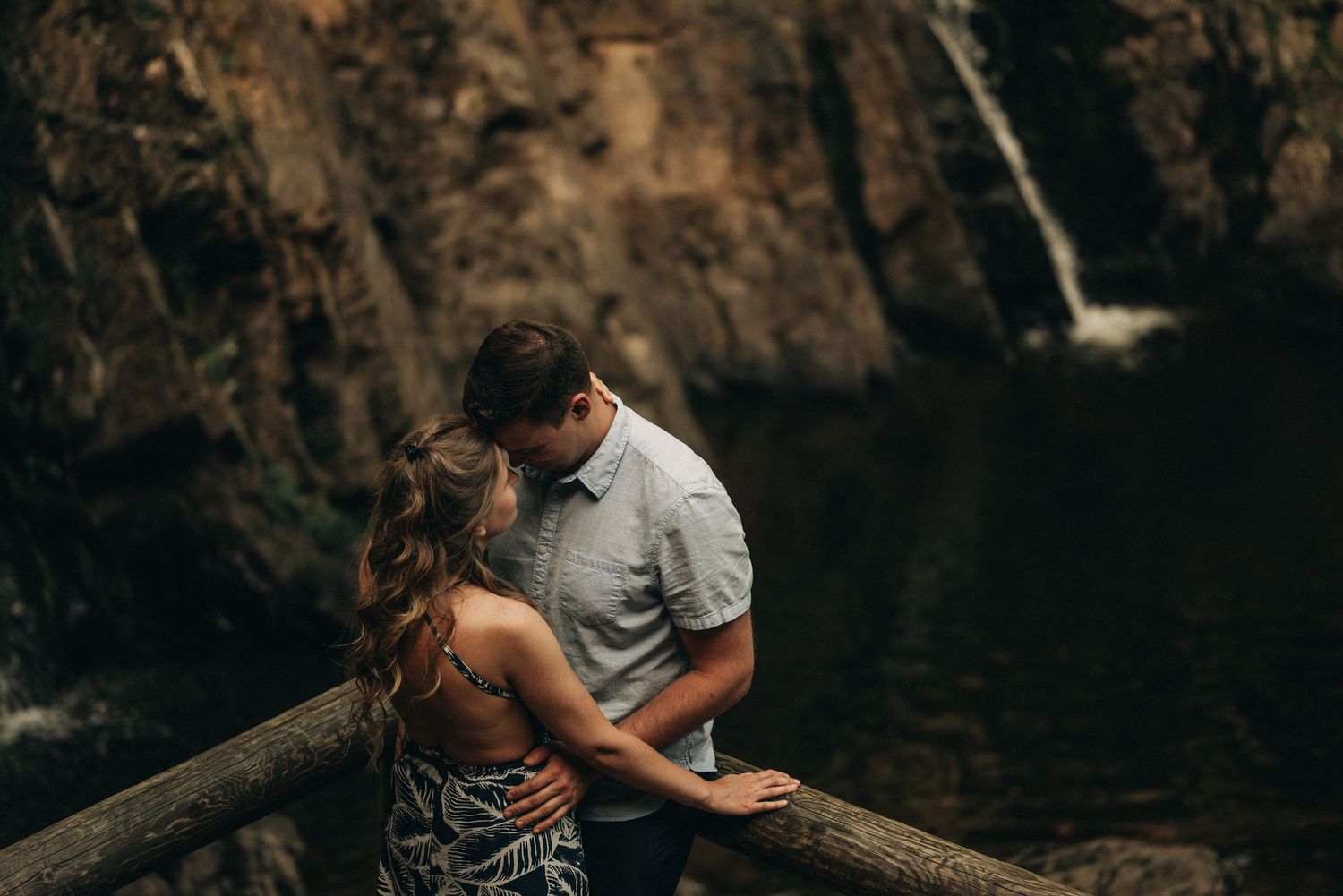 A romantic embrace captured against a dramatic forest waterfall backdrop.