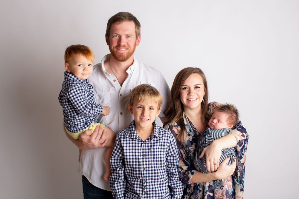A family poses together wearing coordinating blue and white checkered shirts against a light background.