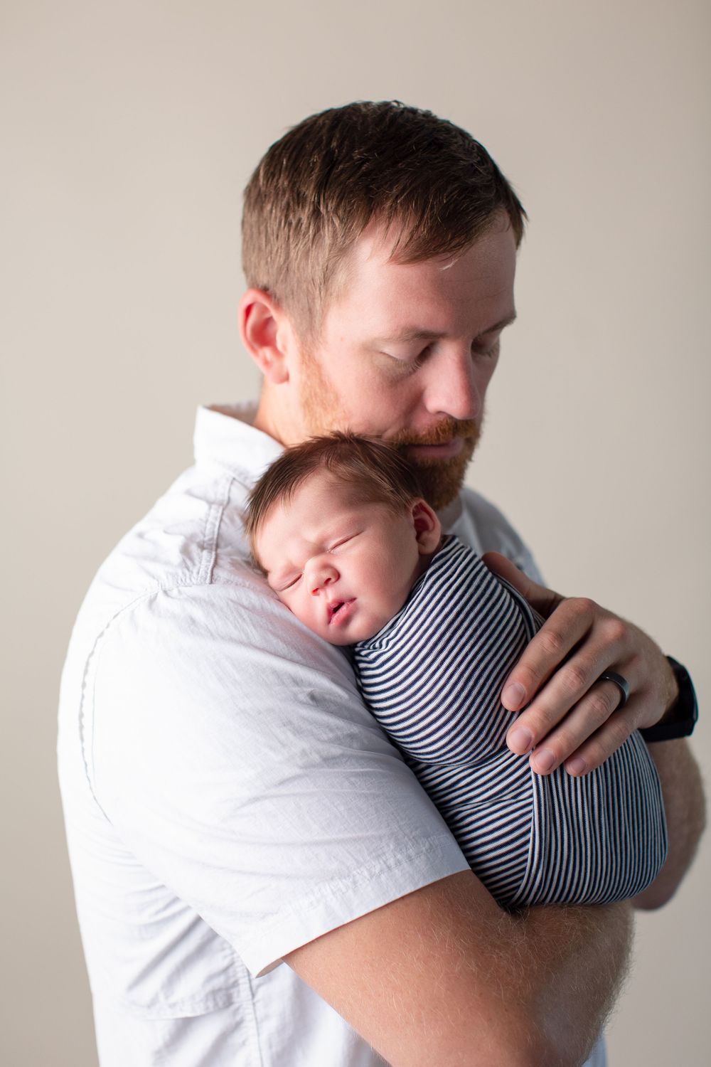 Parent holding sleeping newborn in striped onesie against neutral background.