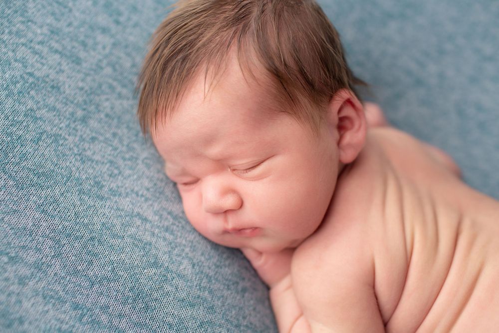 Peaceful newborn resting on textured blue fabric during professional photo shoot.