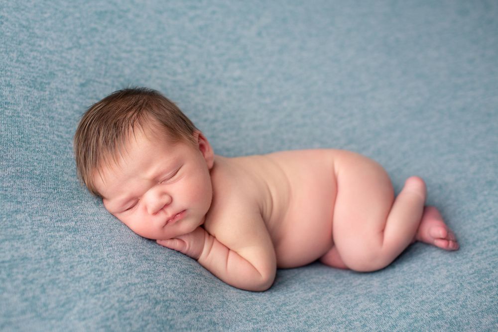 Peaceful newborn baby sleeping on soft blue backdrop during professional portrait session.