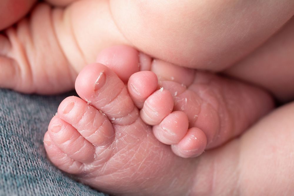 Close-up of tiny newborn baby feet with wrinkled toes on blue fabric.