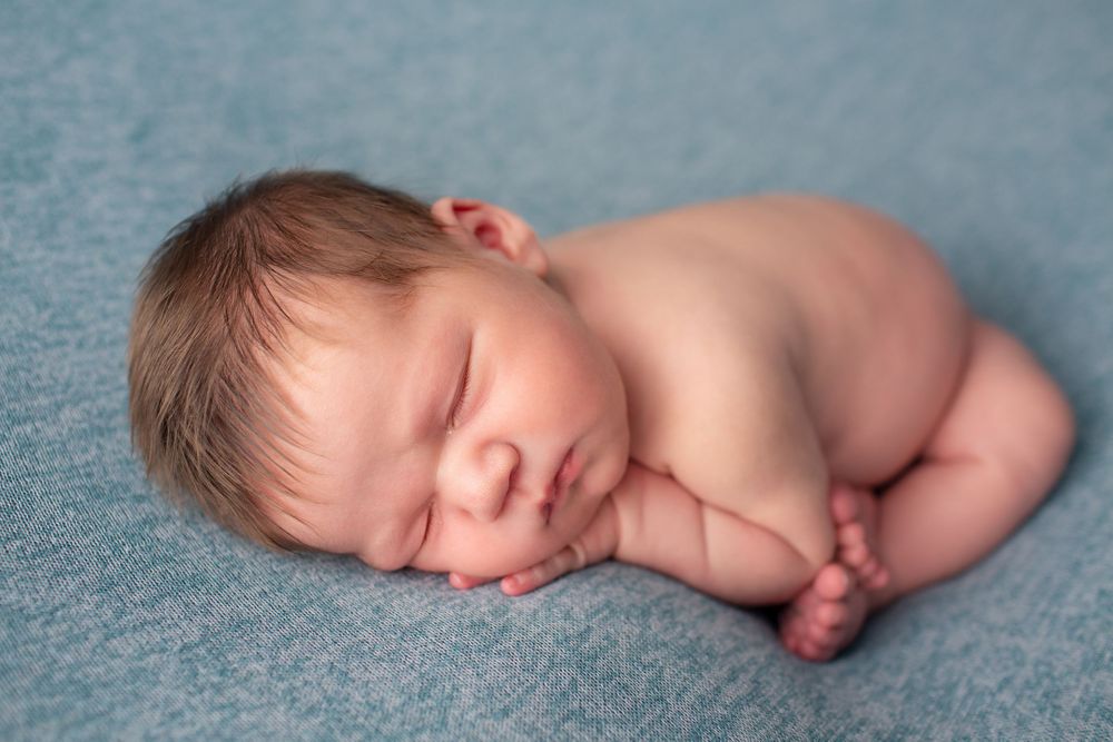 Sleeping baby on blue background during newborn photography session.