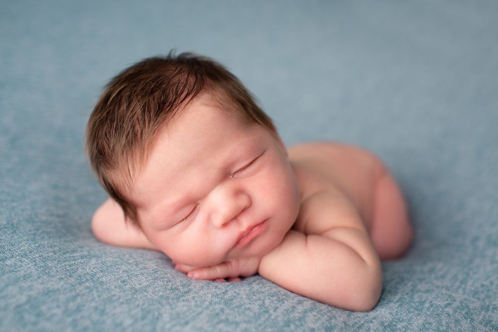 Peaceful newborn sleeping on side against blue backdrop during portrait session.