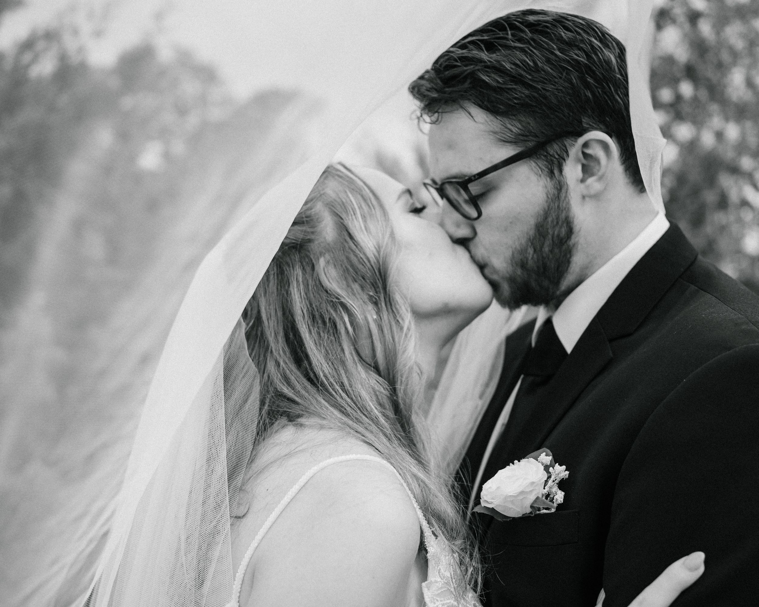 black and white portrait of a bride and groom kissing under a veil