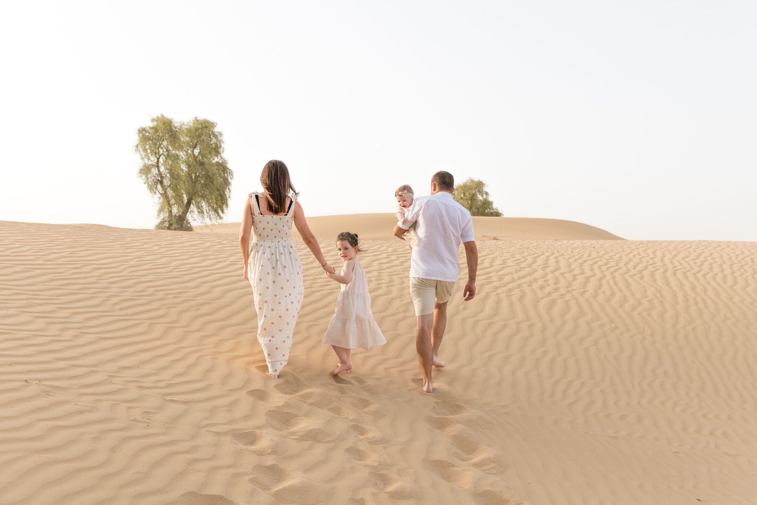 Family walking up a dune in neutral clothing in Dubai desert