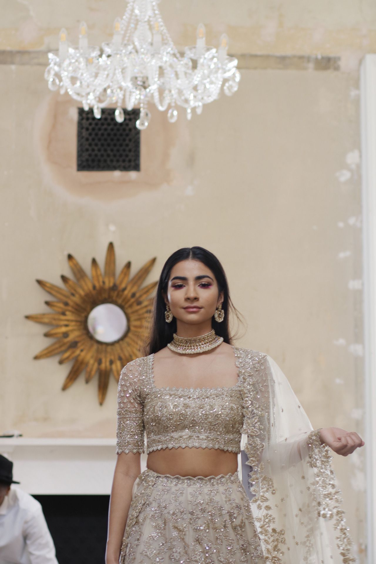 Elegant bridal wear featuring a champagne sequined crop top and lehenga under crystal chandelier.