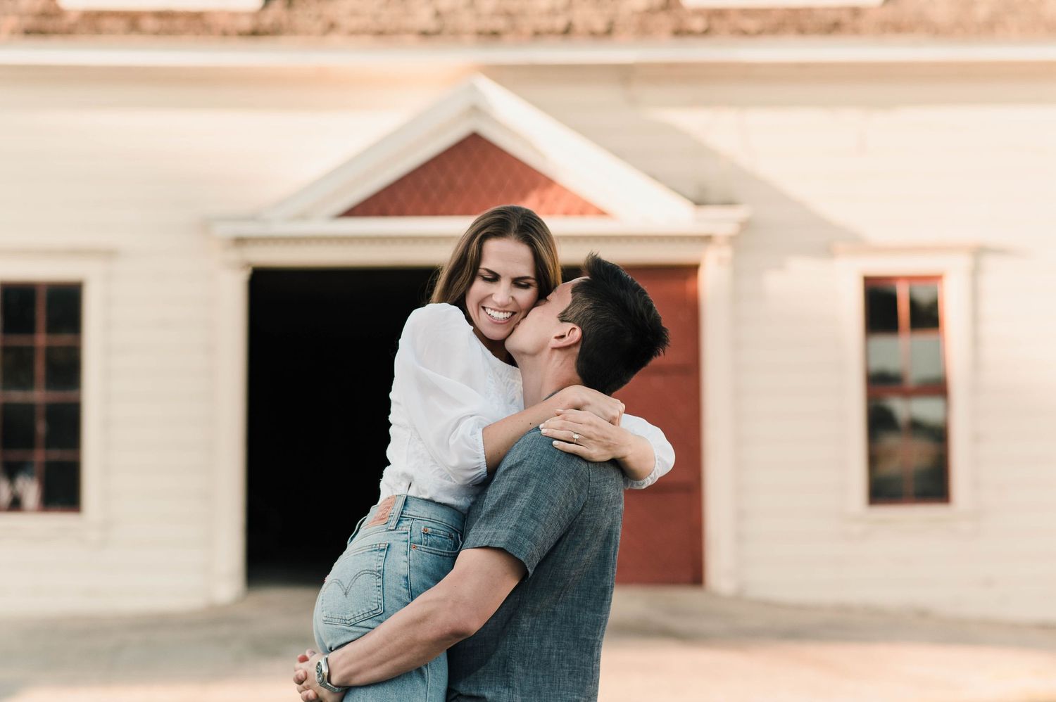 A sweet embrace shared in front of a white colonial style building with red trim.