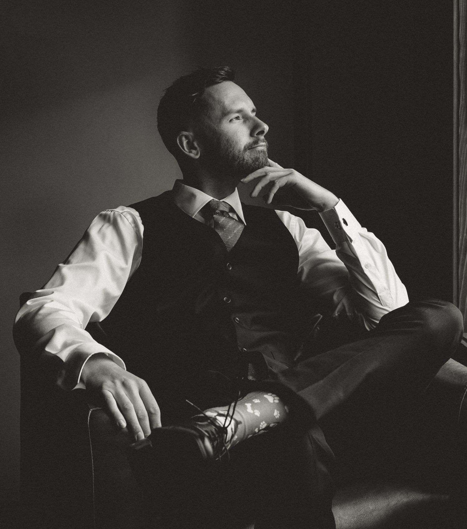 a dapper looking groom gazing out the window of his Canmore hotel, just prior to walking down the aisle with his wife to be.