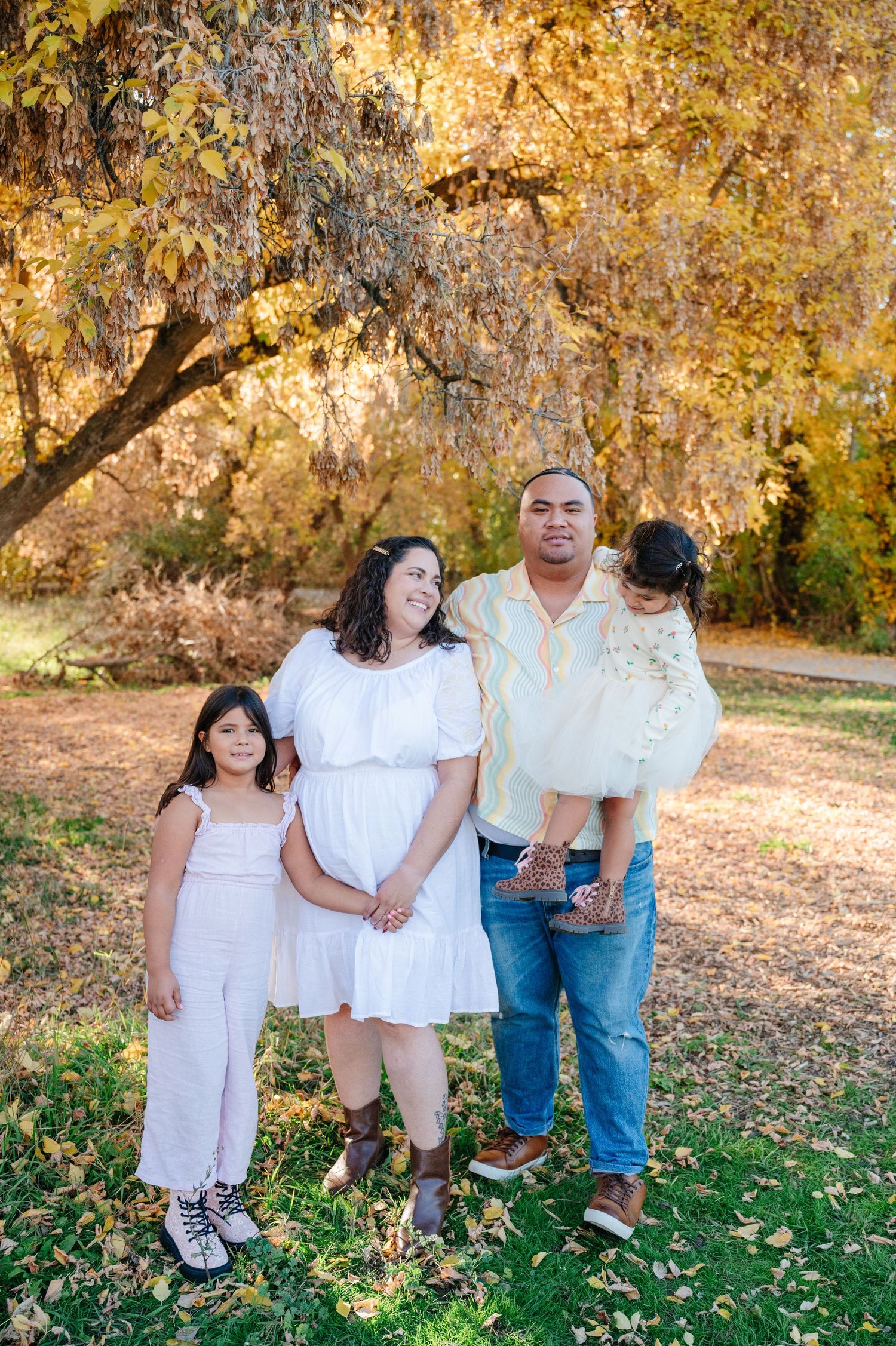 Family of four standing together under golden autumn trees in a park setting.