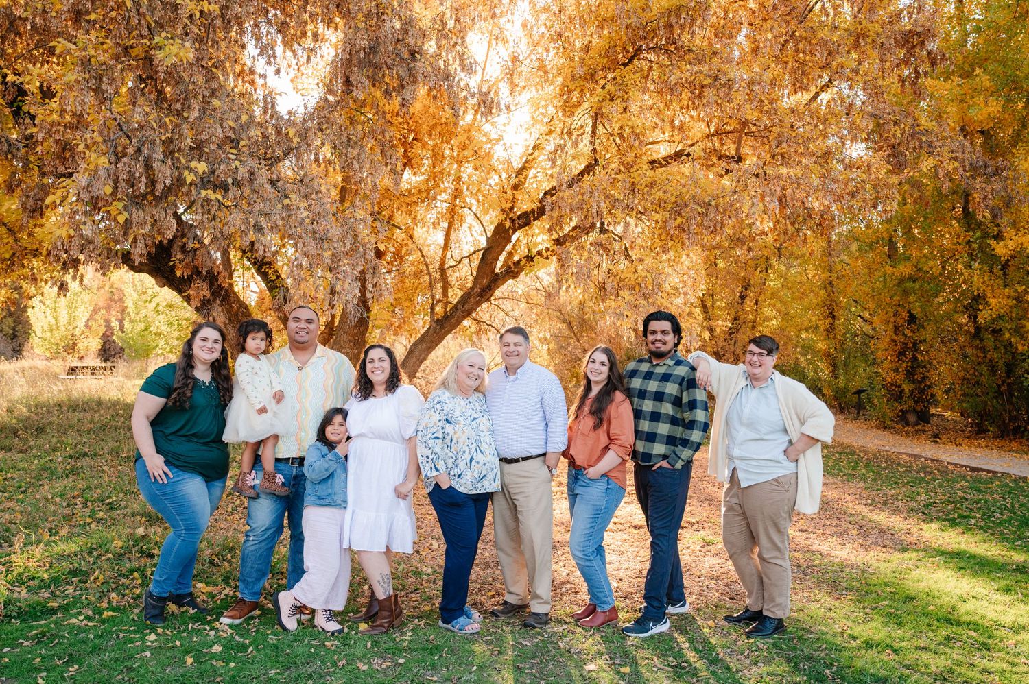 Extended family group poses together on grass under autumn trees with golden lighting.