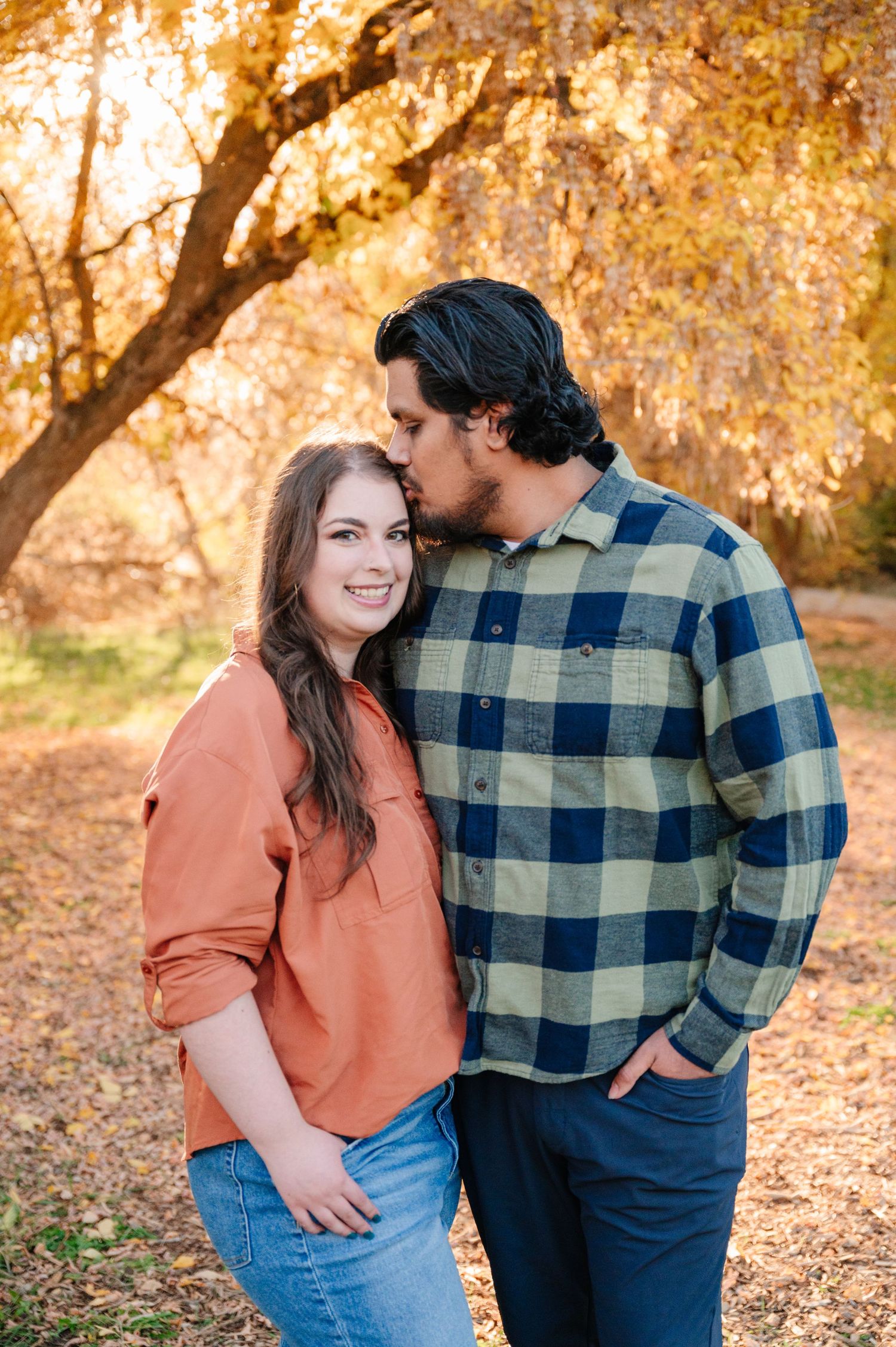 Couple in casual attire sharing an intimate moment under fall foliage.