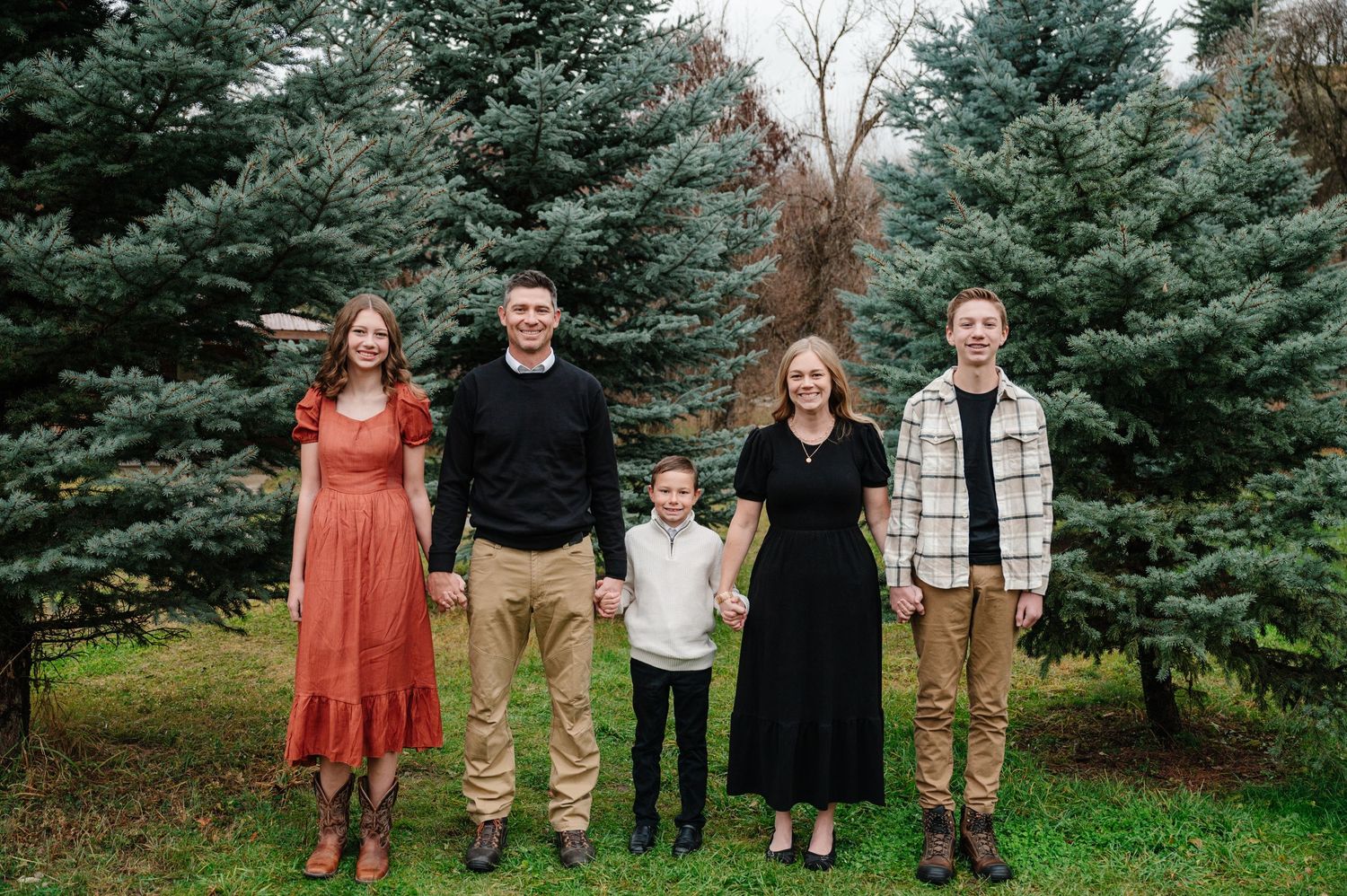 Family of four poses in front of evergreen trees wearing coordinated outfits.