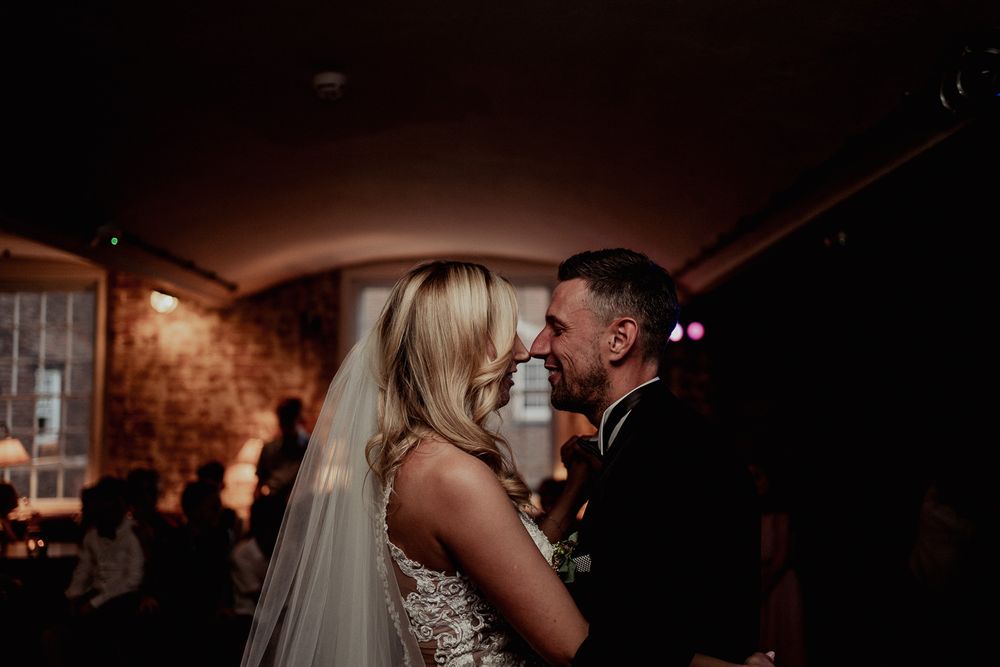 A romantic moment captured between newlyweds during their first dance in a rustic venue.