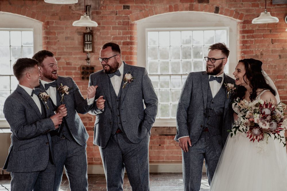 Groomsmen in matching gray suits share laughs and drinks during pre-wedding celebrations.