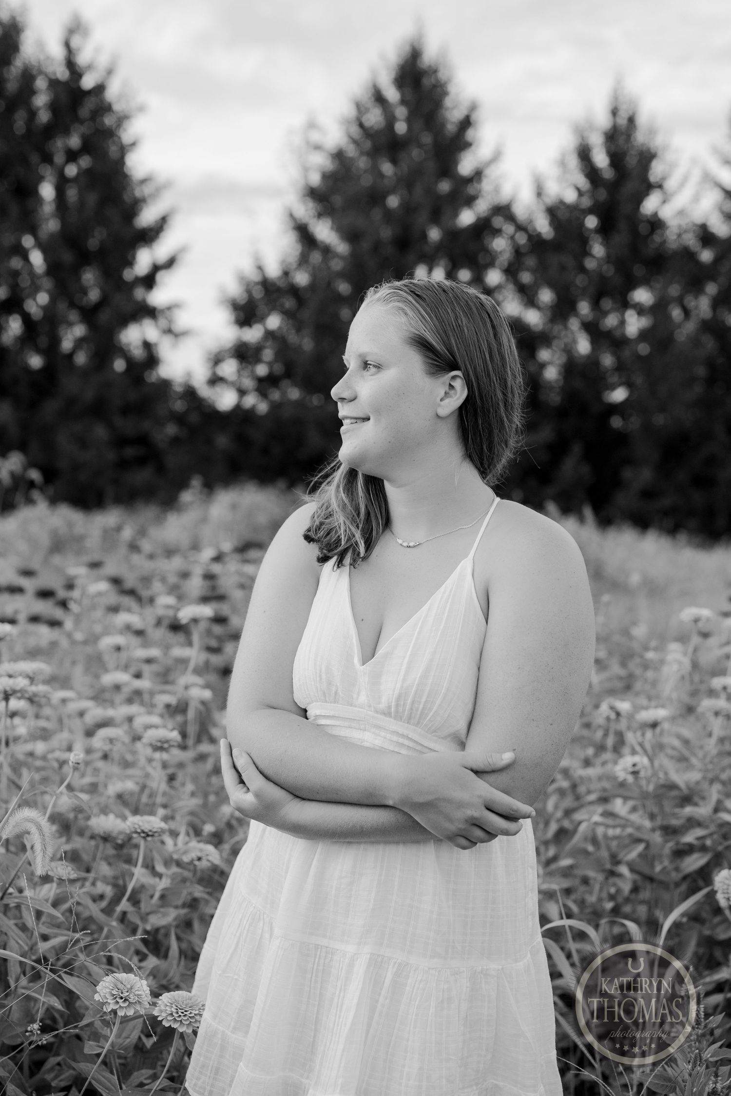 A black and white portrait shot in a wildflower field with pine trees in the background.