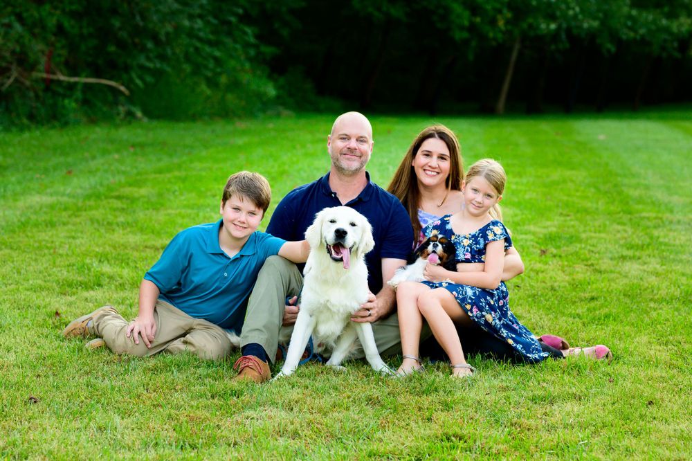 A family and their white Labrador retriever sit together on green grass for a portrait.