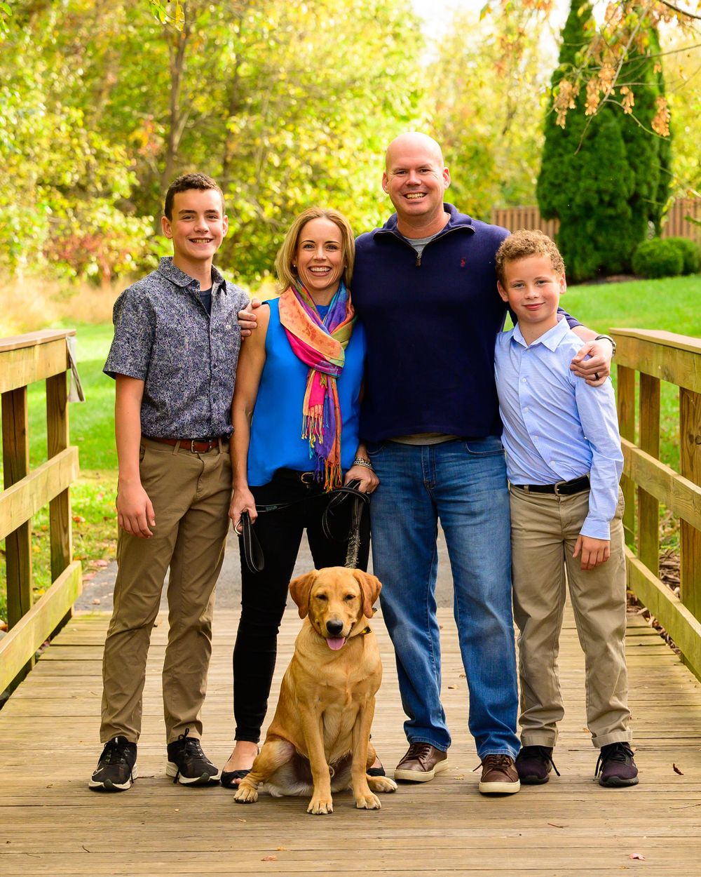 A family with two children and their golden retriever pose together on a wooden bridge.