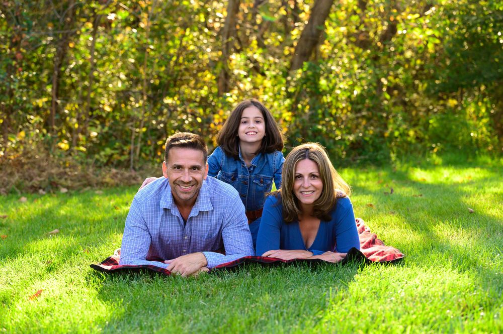 Three people lying on grass together during a sunny outdoor photo session.