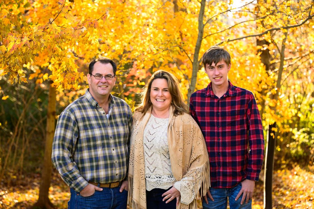 Three people pose together against vibrant yellow autumn foliage.