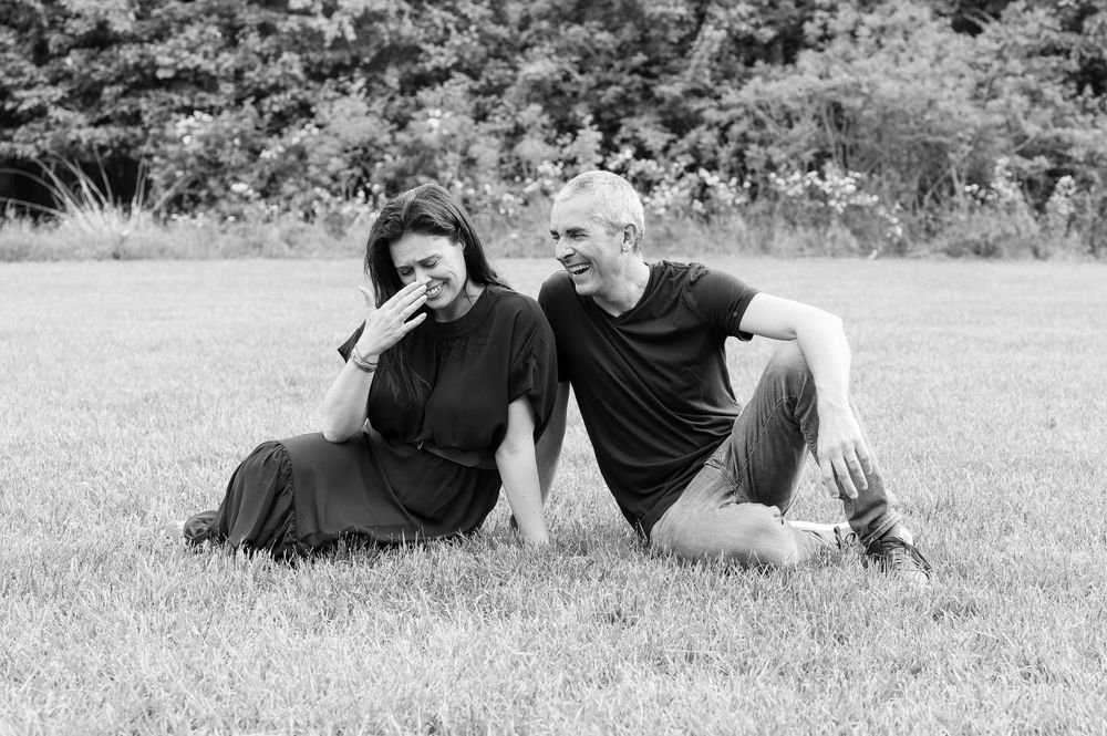 A couple relaxes together on grass in a black and white outdoor portrait.