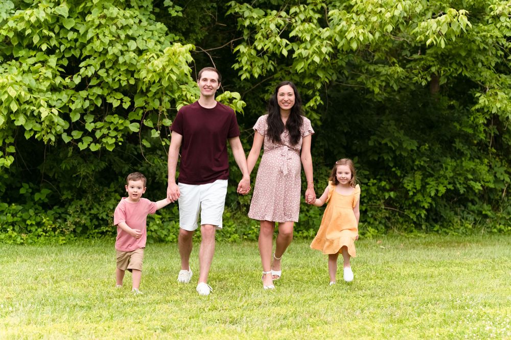 A happy family holding hands while running together through a lush green park.