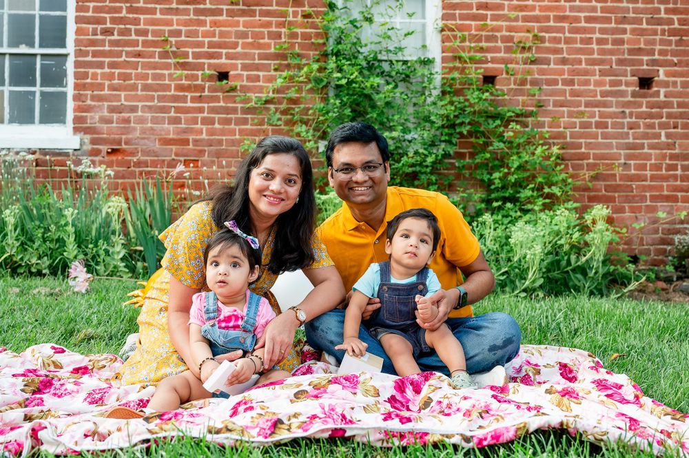 Family portrait on blanket with pink flowers against brick building background.