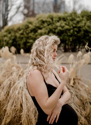 Woman in black dress poses beside ornamental grasses in outdoor setting.