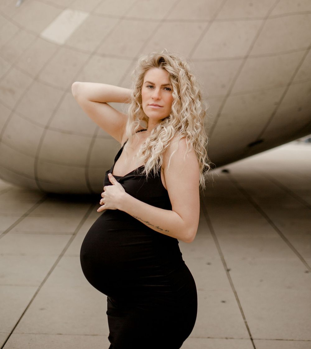 Woman in black dress shows off pregnancy bump against curved architectural background.