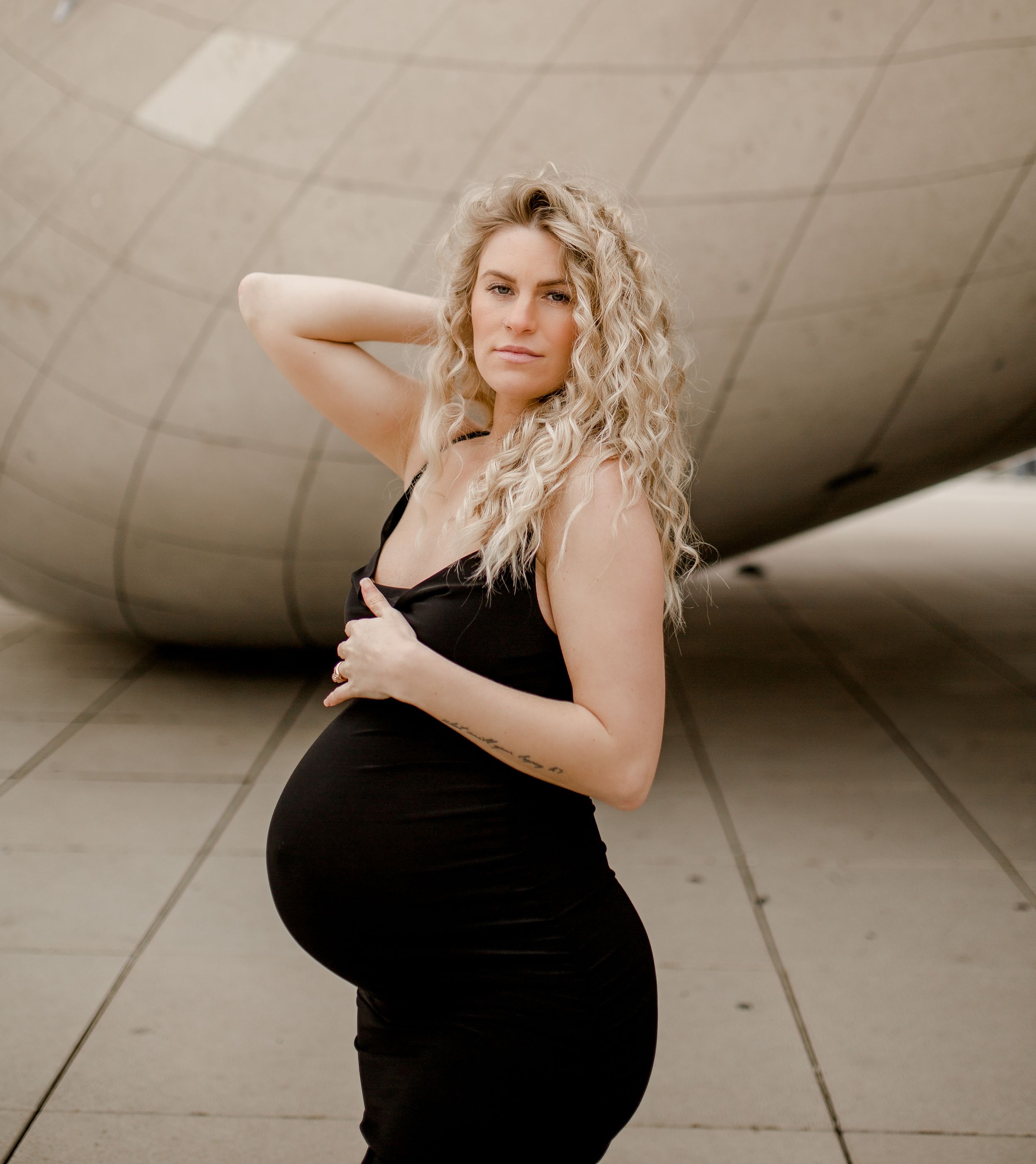 Woman in black dress shows off pregnancy bump against curved architectural background.